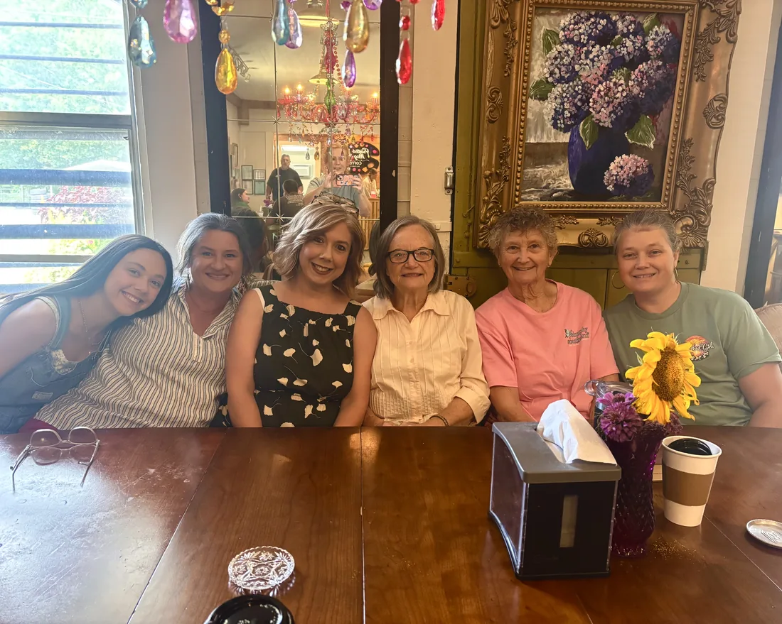 Six ladies of every generation smiling together at the big table at The Painted Mug